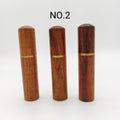 Three warm brown wooden tubes, where a wooden cap is held on with a screw attachment, which looks like a gold band on each, stand upright on a white background. Text above the tubes notes them as 'NO.2'.