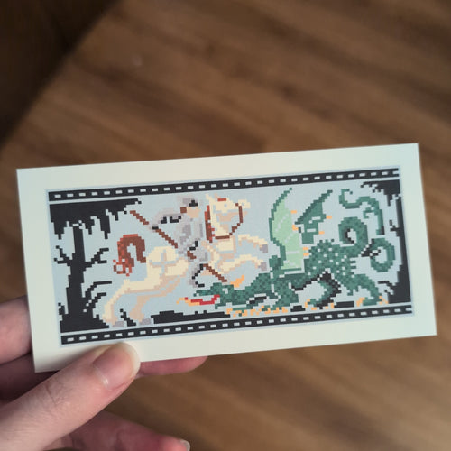 Hand holding a cross-stitch style bookmark picturing a knight fighting a dragon, with wooden flooring in the background.